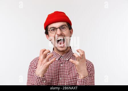 Primo piano ritratto di angosciato e arrabbiato giovane divertente ragazzo hipster con baffi indossare berretto rosso, occhiali, mani di scricchiolio infastidito e fastidioso Foto Stock