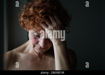 Donna matura per la finestra pensando alla vita Foto Stock