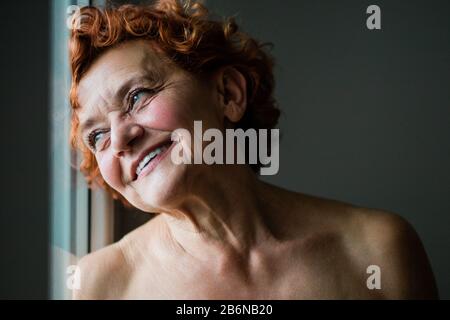 Felice donna matura sorridente dalla finestra Foto Stock
