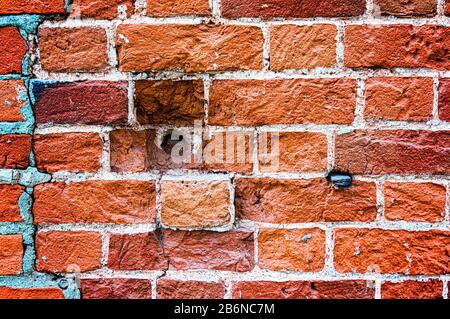 Un vecchio frammento alterato di una parete di mattoni con crepe e fori rotondi. Sfondo per il progettista. Un grande mattone. Foto Stock