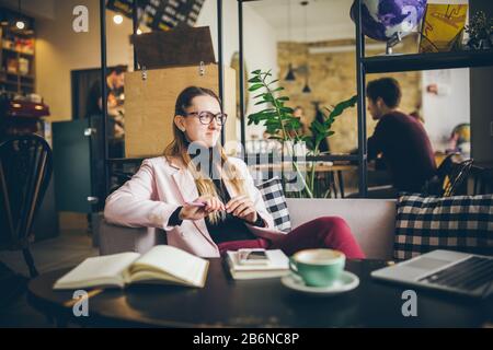 Bella donna caucasica sognando qualcosa mentre si siede con il computer in moderno caffè. Donne freelancer pensare a nuove idee durante il lavoro Foto Stock