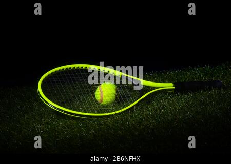 Racchetta da tennis verde con palle da tennis di colore verde su erba con sfondo nero e spazio copia. Foto Stock