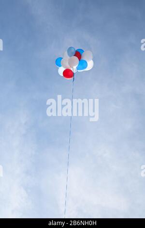 Un mazzo di palloncini rossi, bianchi e blu galleggia in alto contro un cielo blu e nubi oscure. Foto Stock