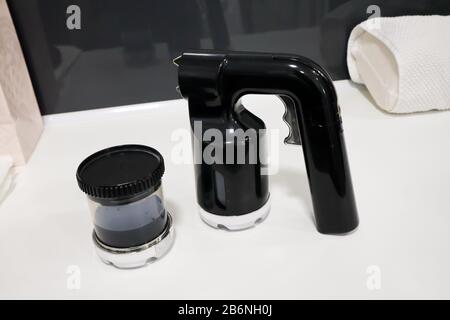 pistola per aerografo isolata con tazza di vernice in plastica per abbronzarsi istantaneamente, vernice spray marrone chiaro per il corpo su tavolo bianco in salone di bellezza professionale Foto Stock