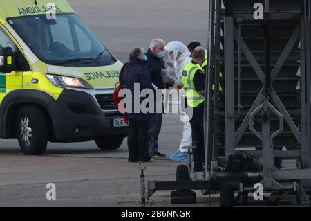 Un membro del NHS West Midlands Ambulance Service, che indossa indumenti protettivi e una maschera facciale, parla ai passeggeri della nave da crociera Grand Princess, colpita dal coronavirus, dopo essere stati rimpatriati dagli Stati Uniti al Regno Unito all'aeroporto di Birmingham. Foto Stock