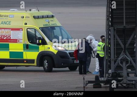 Un membro del NHS West Midlands Ambulance Service, che indossa indumenti protettivi e una maschera facciale, parla a un passeggero della nave da crociera Grand Princess, colpita dal coronavirus, dopo essere stati rimpatriati dagli Stati Uniti al Regno Unito all'aeroporto di Birmingham. Foto Stock