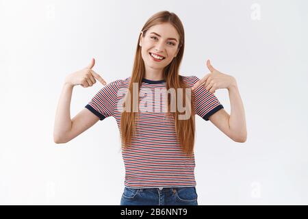 Donna sicura e orgogliosa e astuta con una t-shirt a righe sorridente, testa inclinabile e fotocamera da guardare per promuovere i propri successi Foto Stock