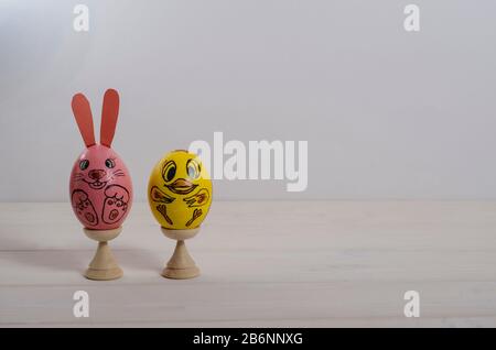 Sfondo carta di Pasqua. Uova di Pasqua sotto forma di coniglio rosa e pollo giallo su sfondo bianco di legno con spazio per le copie. buona pasqua. Laterale Foto Stock