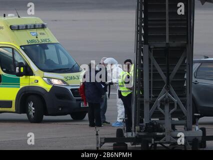 Un membro del NHS West Midlands Ambulance Service, indossando indumenti protettivi e una maschera facciale, parla ai passeggeri (a sinistra) dalla nave da crociera Grand Princess, colpita dal coronavirus, dopo che sono arrivati all'aeroporto di Birmingham dopo il loro rimpatrio nel Regno Unito dagli Stati Uniti. Foto Stock