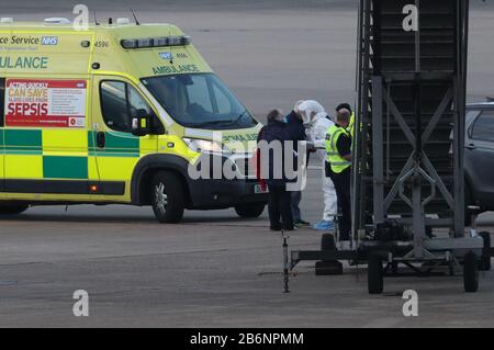 Un membro del NHS West Midlands Ambulance Service, indossando indumenti protettivi e una maschera facciale, parla ai passeggeri (a sinistra) dalla nave da crociera Grand Princess, colpita dal coronavirus, dopo che sono arrivati all'aeroporto di Birmingham dopo il loro rimpatrio nel Regno Unito dagli Stati Uniti. Foto Stock