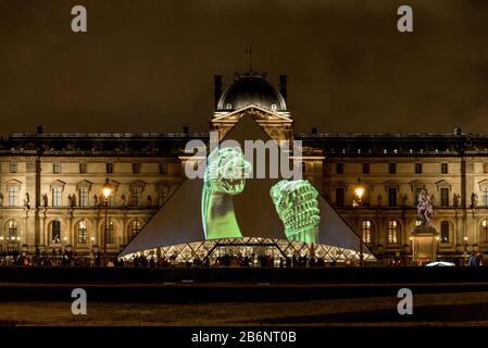 Una presentazione della collezione del Louvre esposta su un ingresso a piramide di vetro in serata, Parigi, Francia Foto Stock