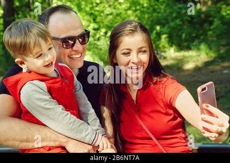 ritratto esterno di una famiglia felice. Mamma, papà e bambino scattano foto selfie. Foto Stock