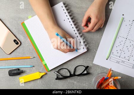 La persona scrive in un notebook su sfondo grigio, vista dall'alto. Concetto di esame Foto Stock