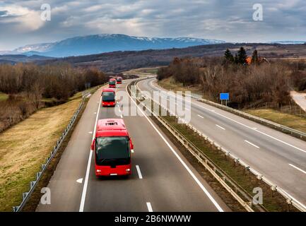 Caravan o convoglio di autobus rossi in linea che viaggiano su un'autostrada di campagna Foto Stock