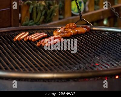 Appetitose e deliziose salsicce si trovano alla griglia di una padella per arrostire al buio. Da sotto la griglia, si bruciano carboni caldi. Rinfreschi festivi all'aperto Foto Stock