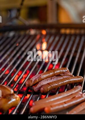 Appetitose e deliziose salsicce si trovano alla griglia di una padella per arrostire al buio. Da sotto la griglia, si bruciano carboni caldi. Rinfreschi festivi all'aperto Foto Stock