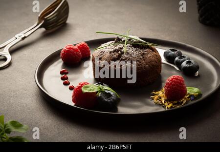 Muffin al cioccolato con lamponi e mirtilli su un piatto nero con retroilluminazione, foto cibo con colori brillanti Foto Stock