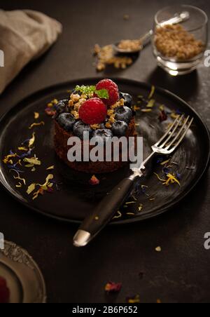 Muffin al cioccolato con lamponi e mirtilli su un piatto nero con retroilluminazione, foto cibo con colori brillanti Foto Stock