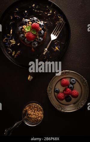 Muffin al cioccolato con lamponi e mirtilli su un piatto nero, stile Moody, foto cibo con colori scuri, vista dall'alto Foto Stock