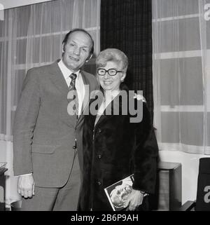 1972, storico, Leggendario campione britannico di pugilato pesante Henry Cooper che si erge per una foto con un fan sorridente e felice, una donna in un cappotto in pelliccia che sta tenendo una copia della sua autobiografia, Catford, South East London, England, UK. Una personalità sportiva molto popolare, Cooper era lui stesso un londinese, essendo nato a Lambeth ed è l'unico pugile ad essere stato assegnato un knighthood. Foto Stock