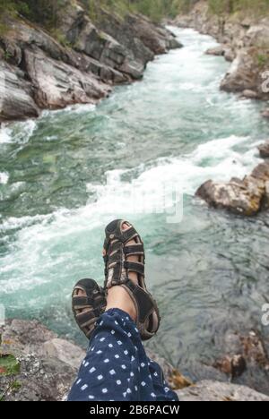 Piedi in scarpe sportive sullo sfondo del turchese fiume di montagna. Primo piano Foto Stock