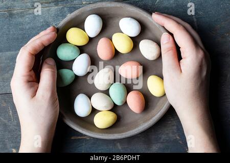 Mani che tengono eleganti uova di pasqua dipinte di pastello in ceramica grigia piastra su vintage vecchio sfondo di legno, buona Pasqua Foto Stock