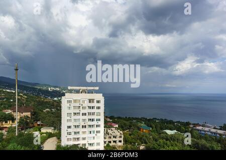 Alto edificio residenziale nel basso villaggio turistico di Alupka. Arcobaleno sul mare in una giornata nuvolosa Foto Stock