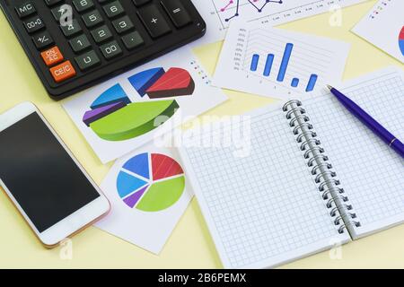 Grafica, notebook, penna, calcolatrice e telefono si trovano su uno sfondo giallo. Business analitico ancora vita Foto Stock