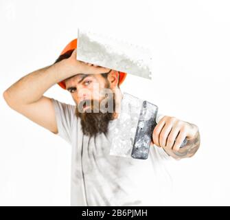 Costruttore in elmetto, casco, operatore barbuto tiene utensili intonacatori, lavorando su sfondo bianco isolato. Uomo con barba con volto serio in stoppino sporco, primo piano, disfocato. Foto Stock