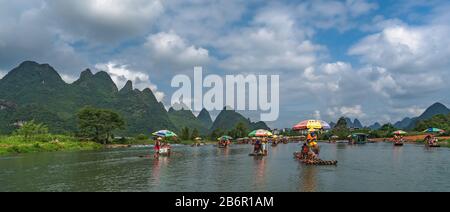 Yangshuo, Cina - Agosto 2019 : Turisti seduti su zattere di bambù guidati da guide con lunghi bastoni sul pittoresco e bellissimo fiume Yulong Foto Stock