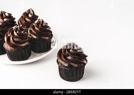 Deliziosi cupcake al cioccolato con glassa al cioccolato e spruzzati d'oro su piastra in porcellana bianca su sfondo bianco isolato. Mockup per il tuo d Foto Stock