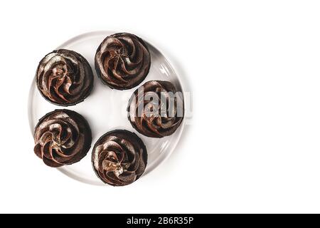 Deliziosi cupcake al cioccolato con glassa al cioccolato e spruzzati d'oro su piastra in porcellana bianca su sfondo bianco isolato. Mockup per il tuo d Foto Stock