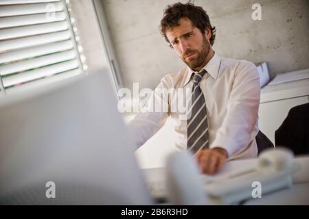 Giovane uomo d'affari adulto che guarda confuso mentre sul computer in un ufficio. Foto Stock