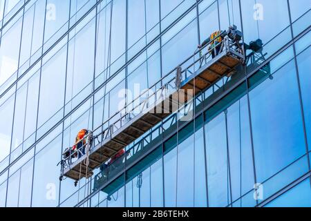 Operai professionali di servizio di pulizia delle finestre in gondola. Due lavoratori utilizzano attrezzature specializzate per accedere e pulire le finestre del grattacielo Foto Stock
