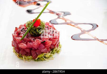 Tartare di tonno fresco, alghe di sesamo, insalata verde e salsa di riduzione balsamica e salsa di frutta tropicale in piatti bianchi Foto Stock