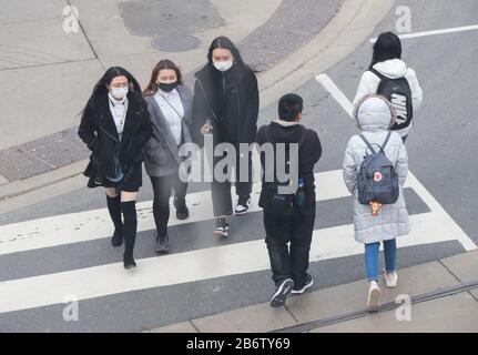 Toronto, Canada. 11th Mar, 2020. Le persone che indossano maschere facciali attraversano la strada alla Chinatown di Toronto, Canada, 11 marzo 2020. Finora in Canada sono stati segnalati almeno 93 casi confermati di COVID-19 e un decesso. Credit: Zou Zheng/Xinhua/Alamy Live News Foto Stock