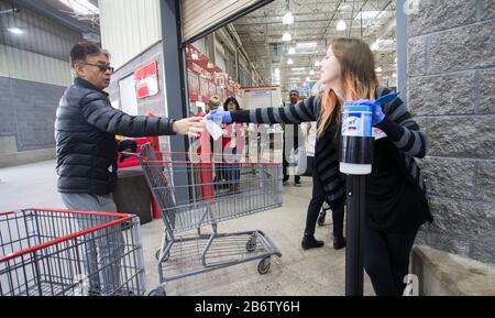 Toronto, Canada. 11th Mar, 2020. Un membro dello staff (R) passa una salvietta a un cliente all'ingresso di un magazzino Costco a Toronto, Canada, 11 marzo 2020. Finora in Canada sono stati segnalati almeno 93 casi confermati di COVID-19 e un decesso. Credit: Zou Zheng/Xinhua/Alamy Live News Foto Stock