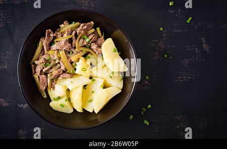 Stufato di manzo, pezzi di manzo stufati con cetriolo decapato in stile russo. Stroganoff di manzo e patate bollite. Vista dall'alto, in alto, in piano Foto Stock