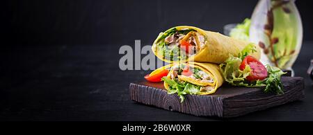 Tortilla fresca avvolge con pollo e verdure fresche su tavola di legno. Burrito di pollo. Cucina messicana. Banner Foto Stock