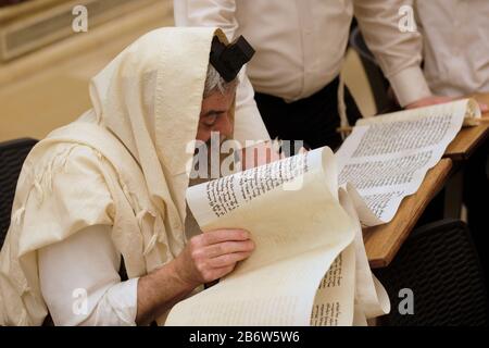 L'ebreo ultra ortodosso avvolto con lo scialle di Talit e le filatere di tefillin leggono la Megillah o il rotolo di Esther durante il festival ebraico di Purim nella città vecchia Gerusalemme est Israele Foto Stock