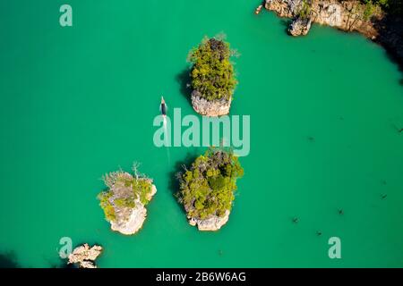 Vista dall'alto di una barca a coda lunga che passa tra enormi dita di pietra calcarea su un lago (lago Cheow Lan, Thailandia) Foto Stock