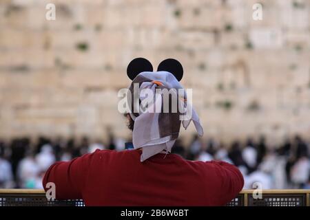 Una donna ebrea che indossa Mickey mouse orecchie costume guardando su recinzione in metallo perforato che divide maschio e femmina sezione di preghiera al muro occidentale o Wailing Wall Old City East Jerusalem Israel Foto Stock