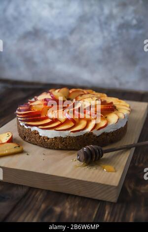 Cheesecake fatto in casa con pesche. Dessert di frutta salutare con formaggio spalmabile, nettarine, miele e timo su tavola di legno. Torta dietetica Foto Stock