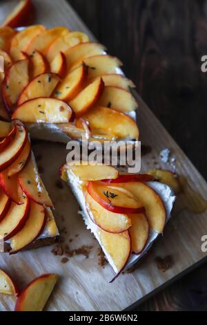 Cheesecake fatto in casa con pesche. Dessert di frutta salutare con formaggio spalmabile, nettarine, miele e timo su tavola di legno. Torta dietetica Foto Stock