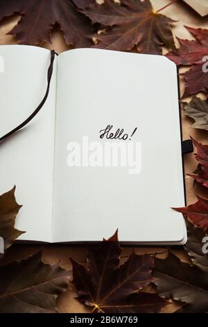 La parola ciao in blocco note e foglia di acero. Ciao concetto autunno Foto Stock
