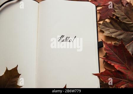 La parola ciao in blocco note e foglia di acero. Ciao concetto autunno Foto Stock