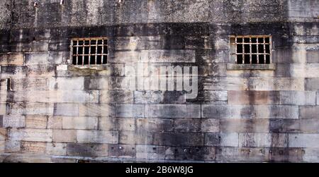 Edificio storico in pietra arenaria del carcere costruito in mattoni, finestre arrugginite griglia di sicurezza, parete di fondo Foto Stock