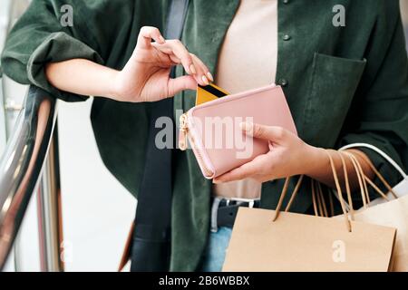 Primo piano di donna irriconoscibile in camicia che tiene borse di carta e ottenere carta di credito fuori dalla borsa Foto Stock