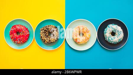 4 ciambelle fresche e appetitose adagiate su un piatto di sfondo giallo e blu. Foto Stock