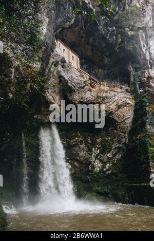 Il santuario di Covadonga è stato costruito all'interno della montagna con la cascata sottostante Foto Stock